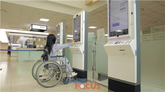 배리어프리 키오스크를 도입한 병원에서 휠체어 장애인이 기기를 작동하는 사진